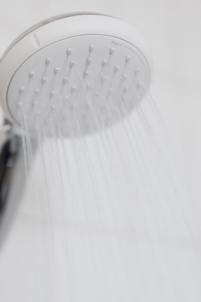 The Art of Drawing Readers In: Your attractive post title goes here Close-up of a modern shower head with water streaming in a white bathroom setting.