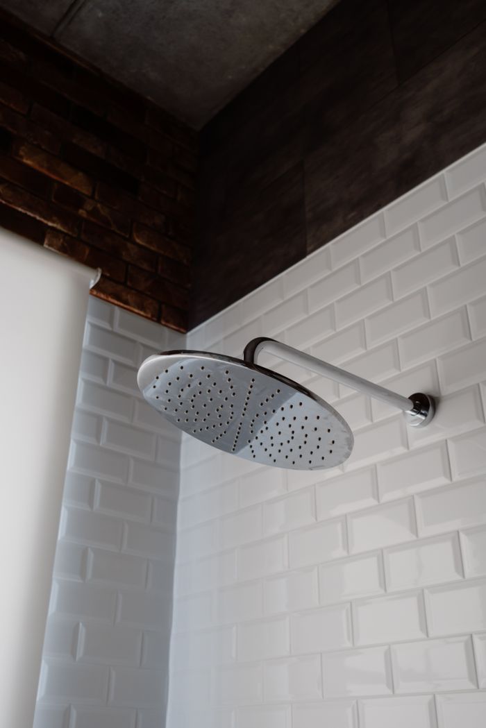 Mastering the First Impression: Your intriguing post title goes here Sleek stainless steel shower head set against a stylish bathroom with white tiles and a brick accent wall.